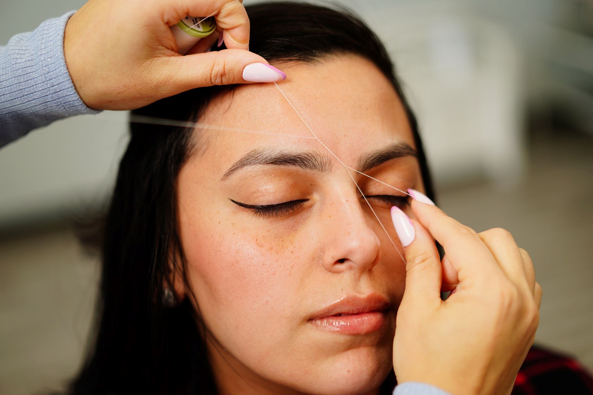 A picture of a woman's face being threaded. Photo Credit: Shutter Glee Photography